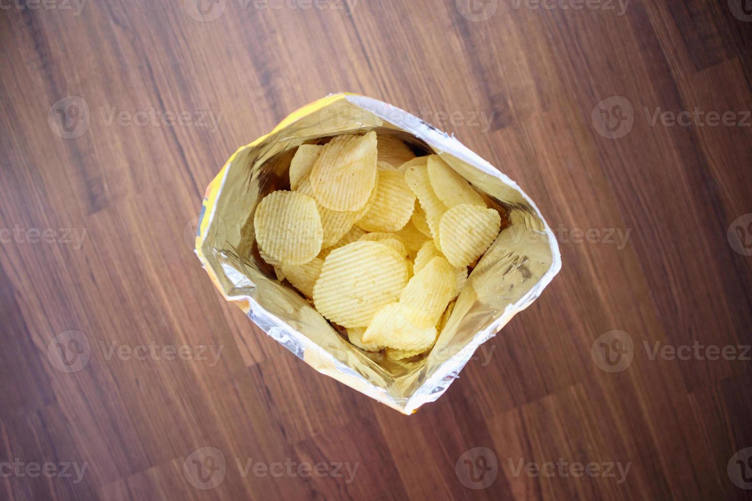 Potato chips in open snack bag close up on table floor photo