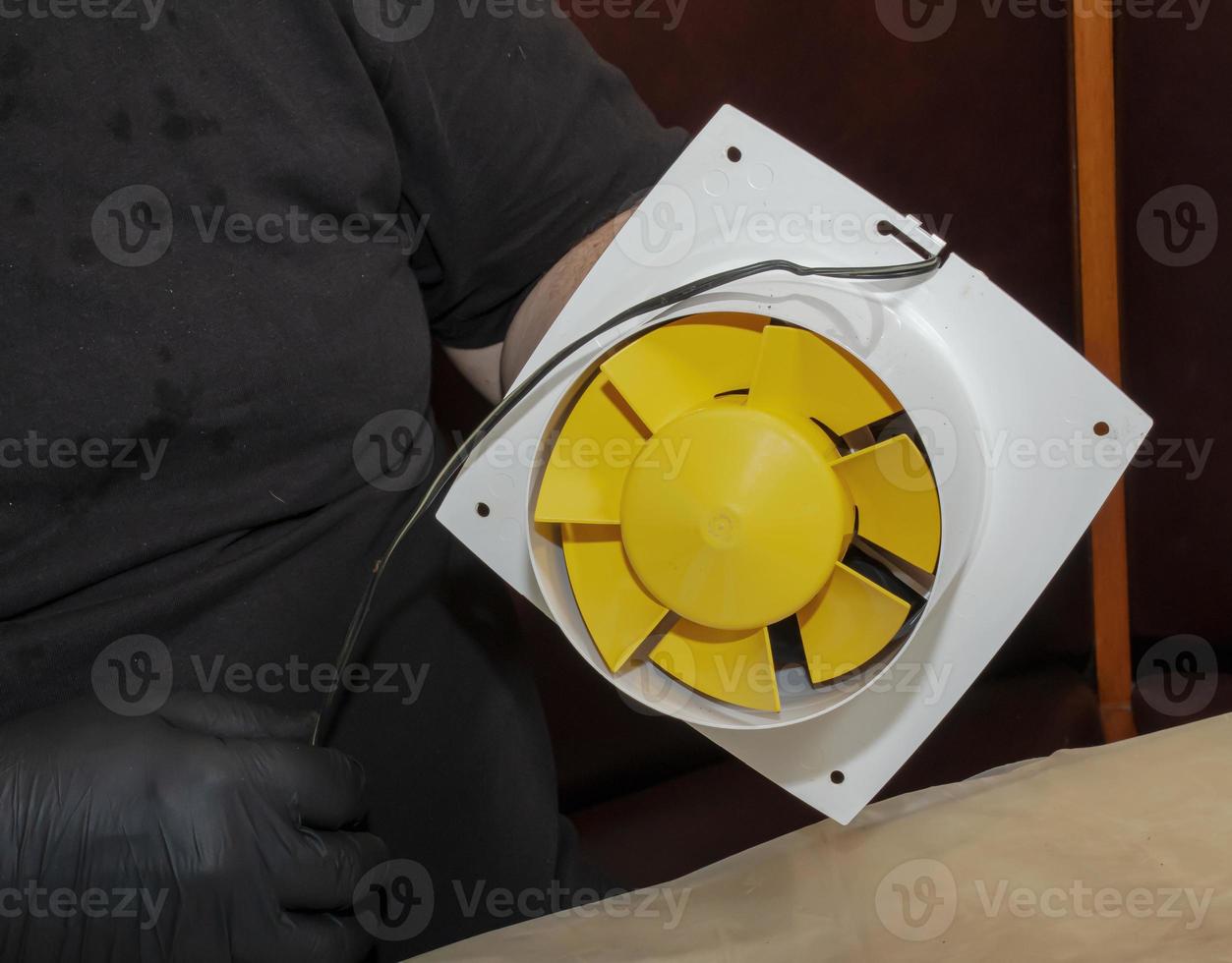 The process of assembling the kitchen exhaust fan after cleaning the wash. A man works with a screwdriver in his hands photo