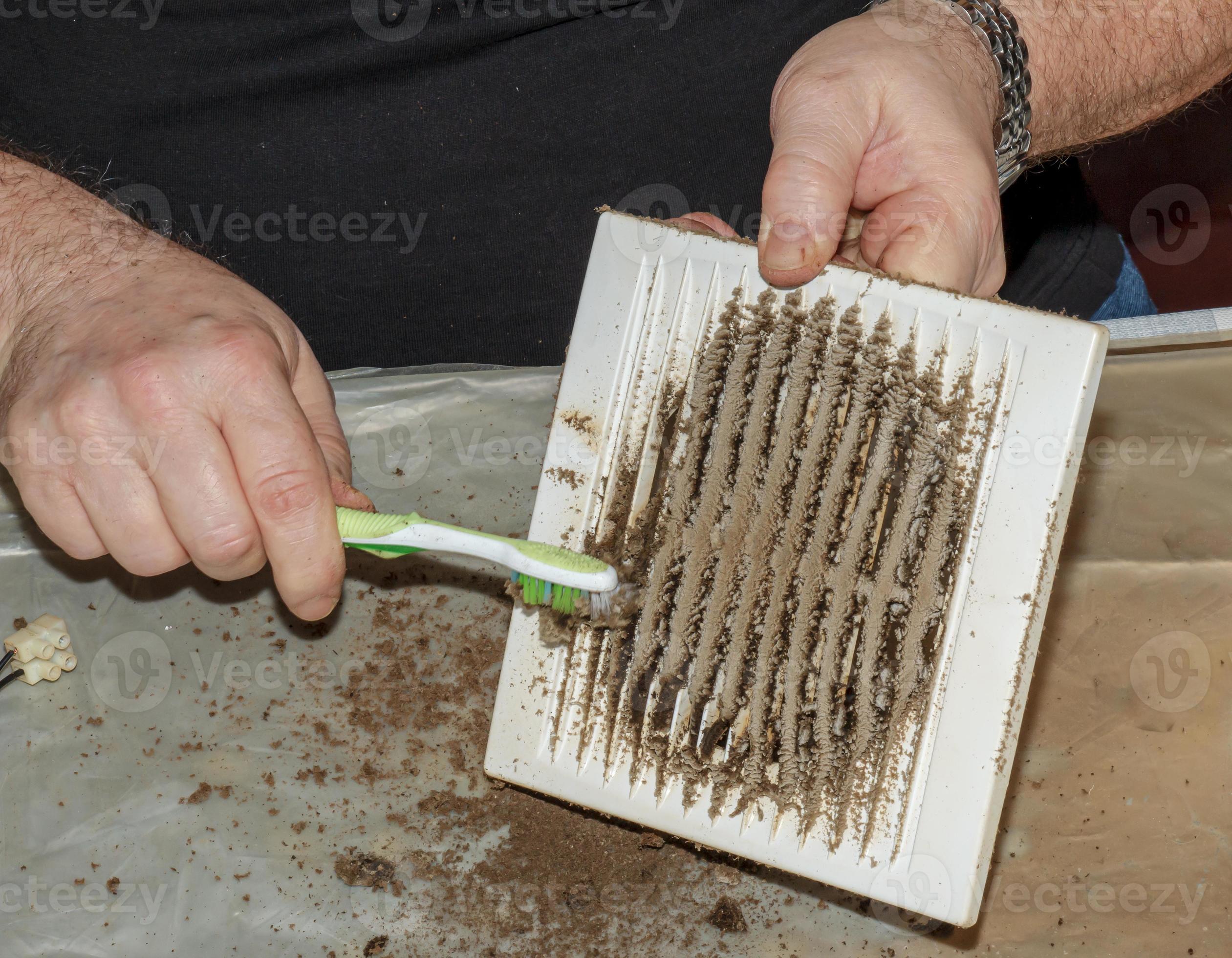 Cleaning a very dirty kitchen exhaust fan from dirt with a brush. A man cleans the parts of a