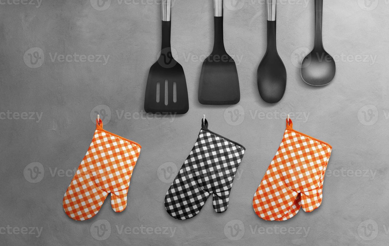 Orange Heat Resistant Cooking Gloves Black with kitchen utensils hanging on cement wall. photo