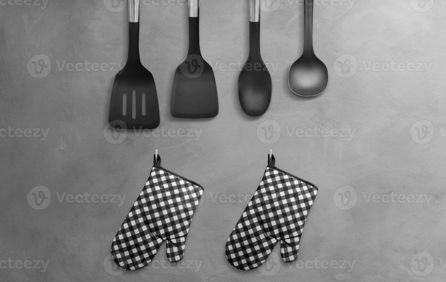 Black heat resistant cooking gloves with kitchen utensils hanging on a cement wall. photo