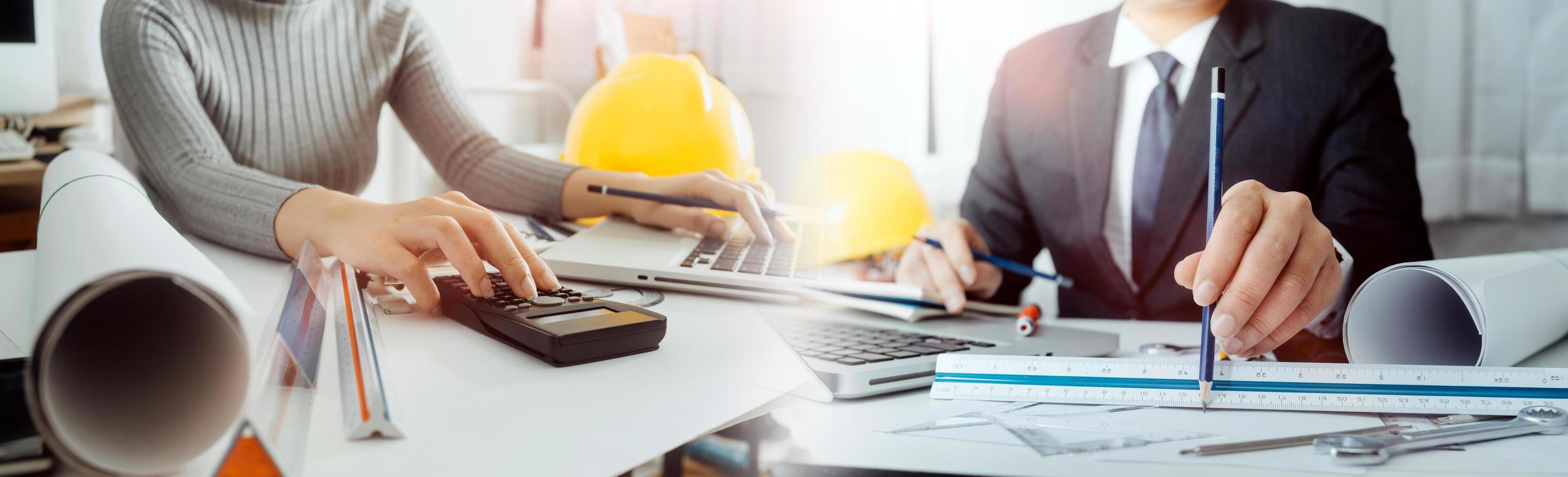 Two colleagues discussing data working and tablet, laptop with on on architectural project at construction site at desk in office photo