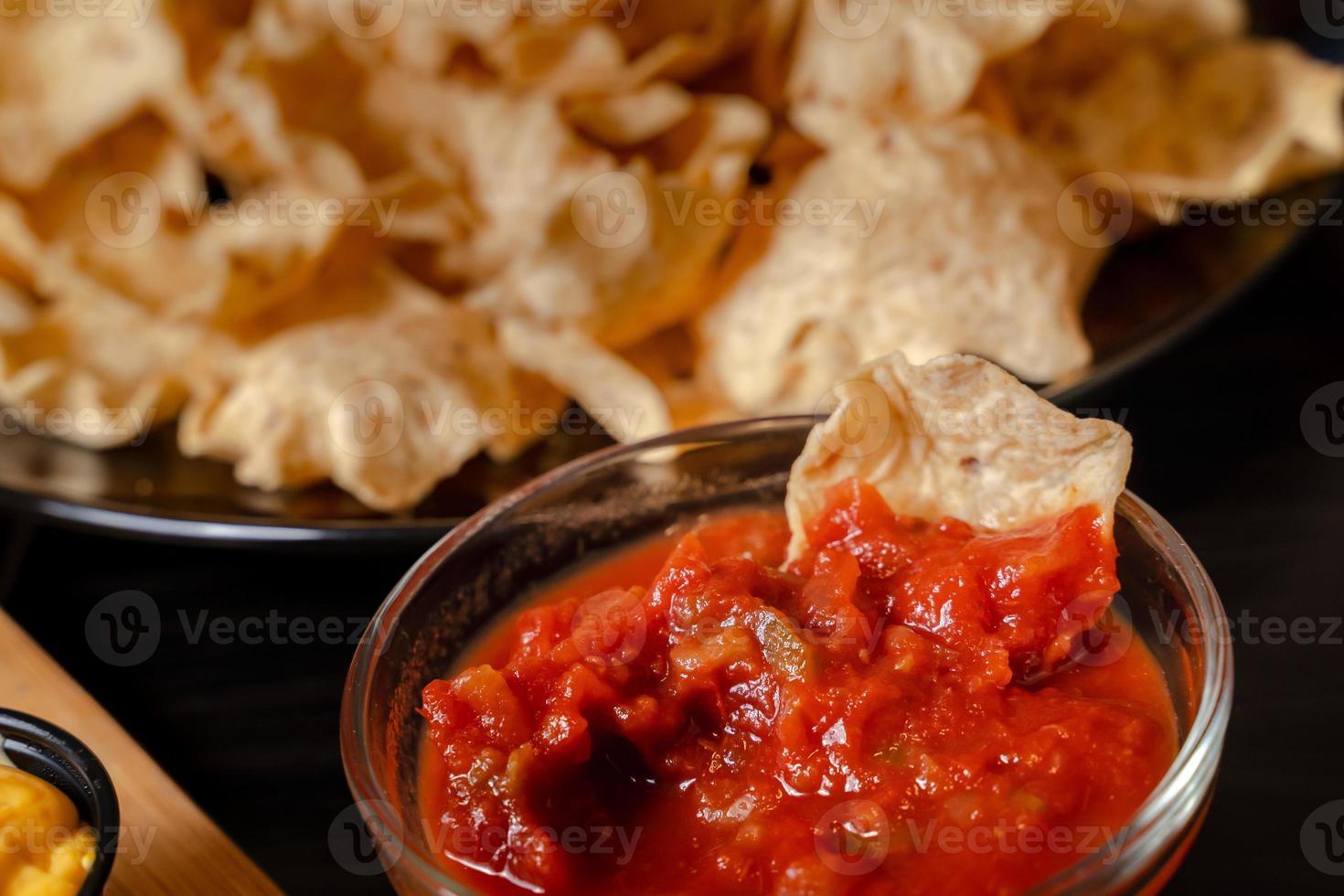 Close up Hand hold chip dip tomato salsa with plate with taco, nachos chips and tomato dip. Spicy Nachos  on rustic wooden background photo