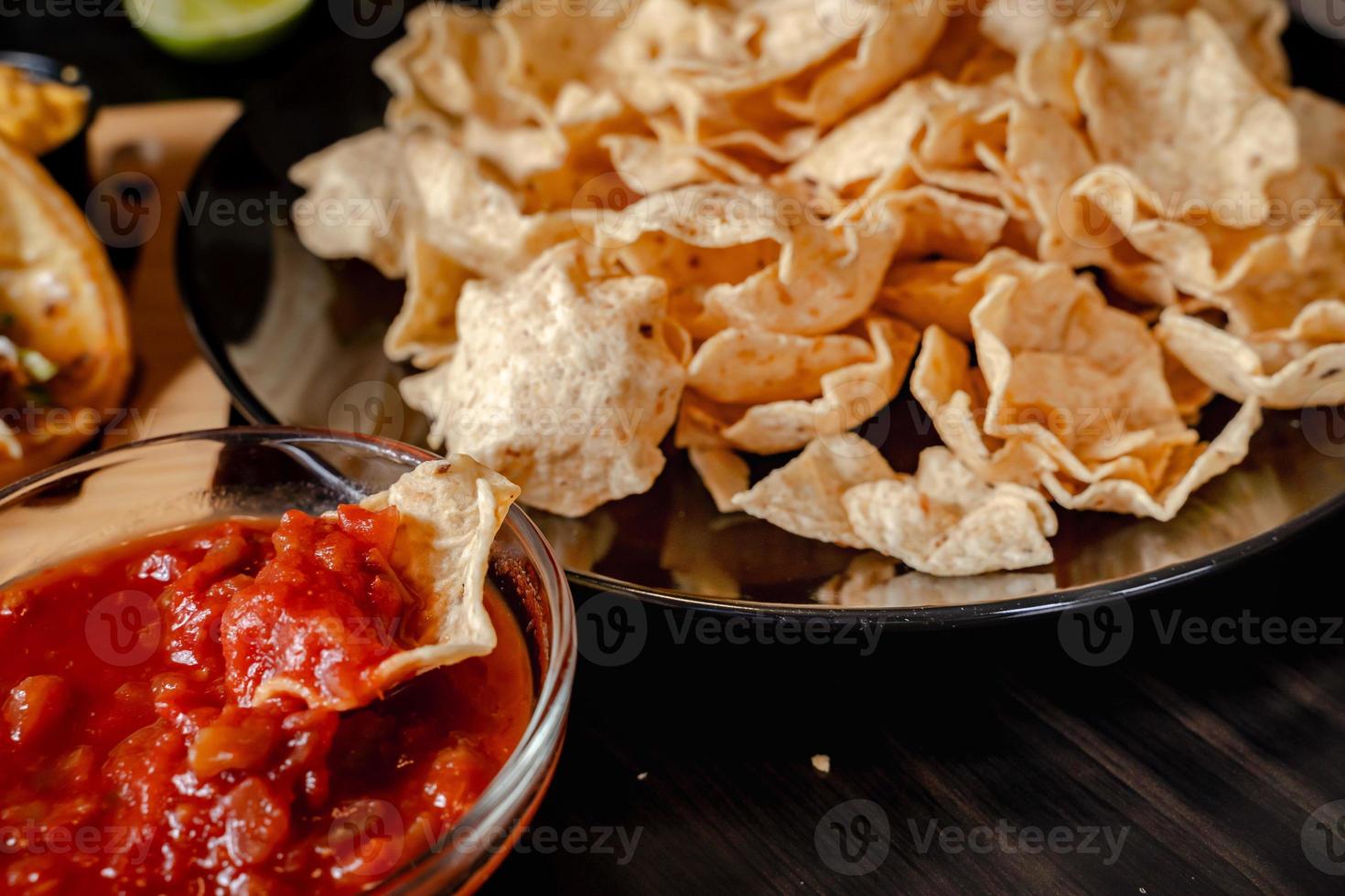 Close up Hand hold chip dip tomato salsa with plate with taco, nachos chips and tomato dip. Spicy Nachos  on rustic wooden background photo
