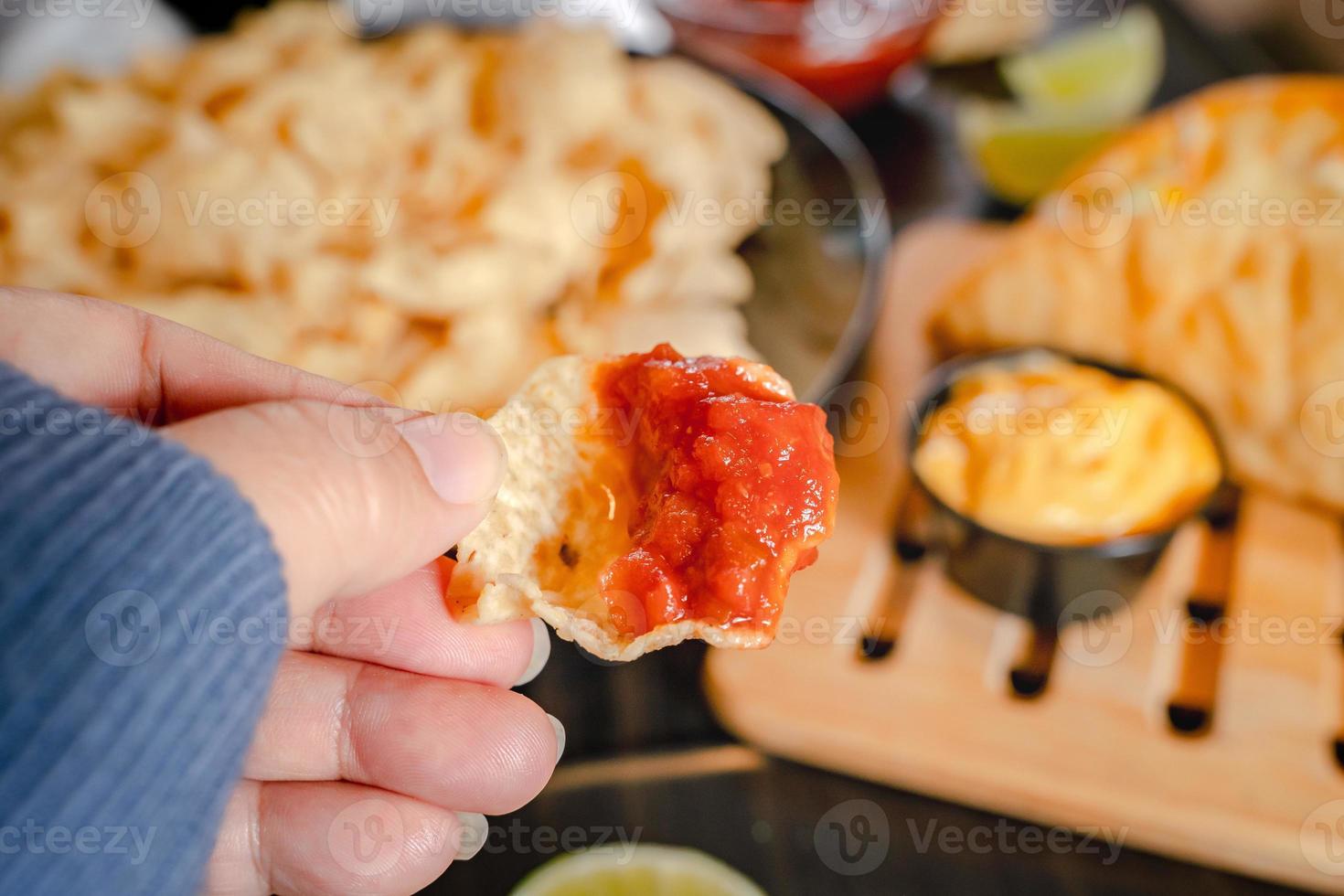 Close up Hand hold chip dip tomato salsa with plate with taco, nachos chips and tomato dip. Spicy Nachos  on rustic wooden background photo
