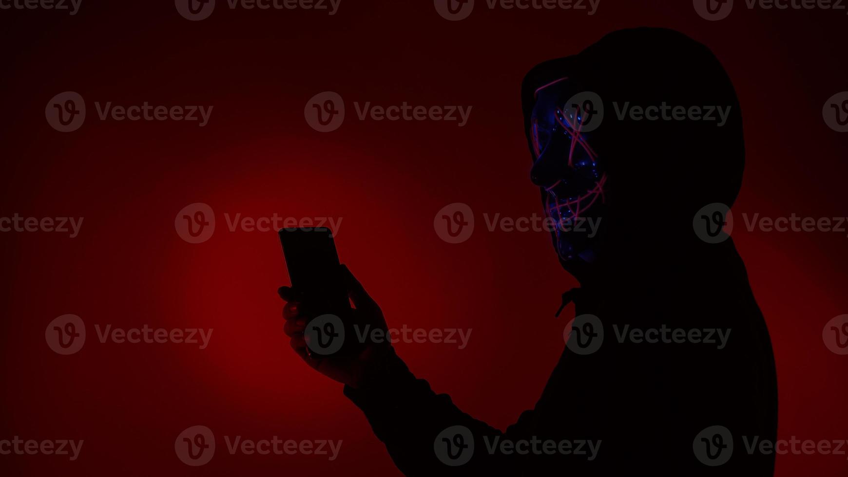 Digital security Concept. Anonymous hacker with mask holding smartphone hacked. photo