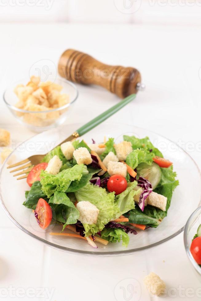 ensalada fresca con tomates cherry, zanahoria, lechuga romana y lechuga en un plato sobre fondo blanco de madera foto