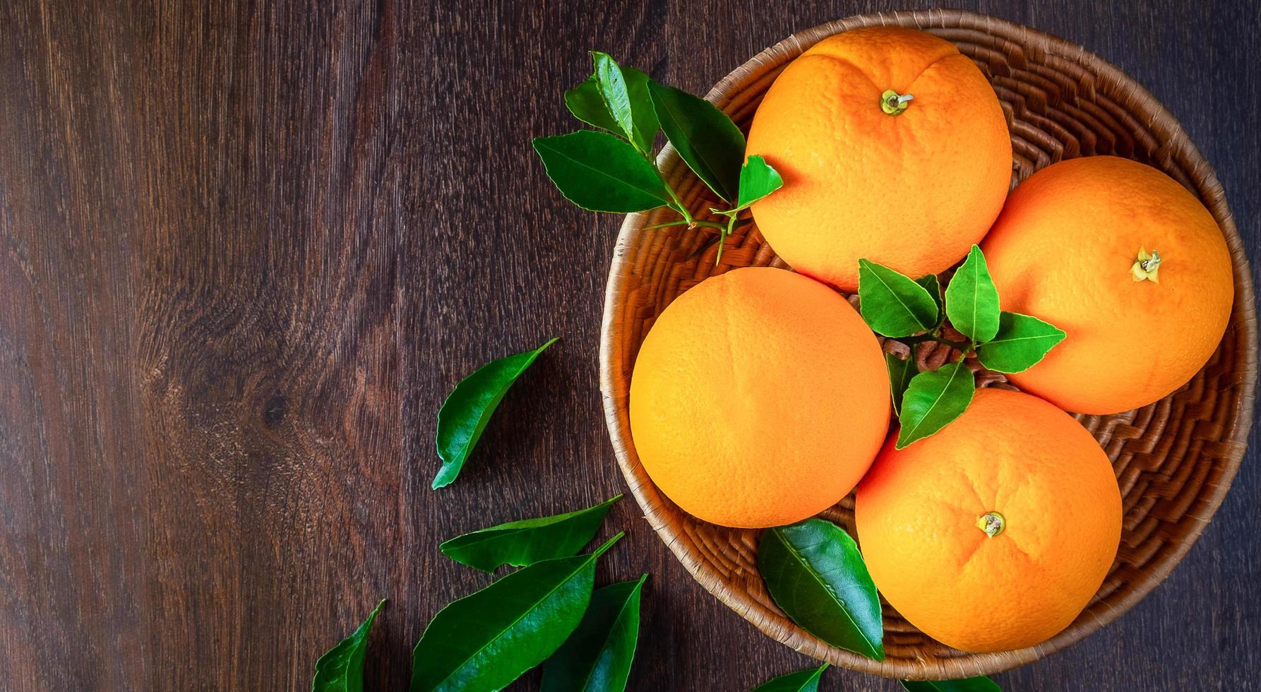 Top view of fresh orange fruit  in the basket and orange leaf on the wooden background photo