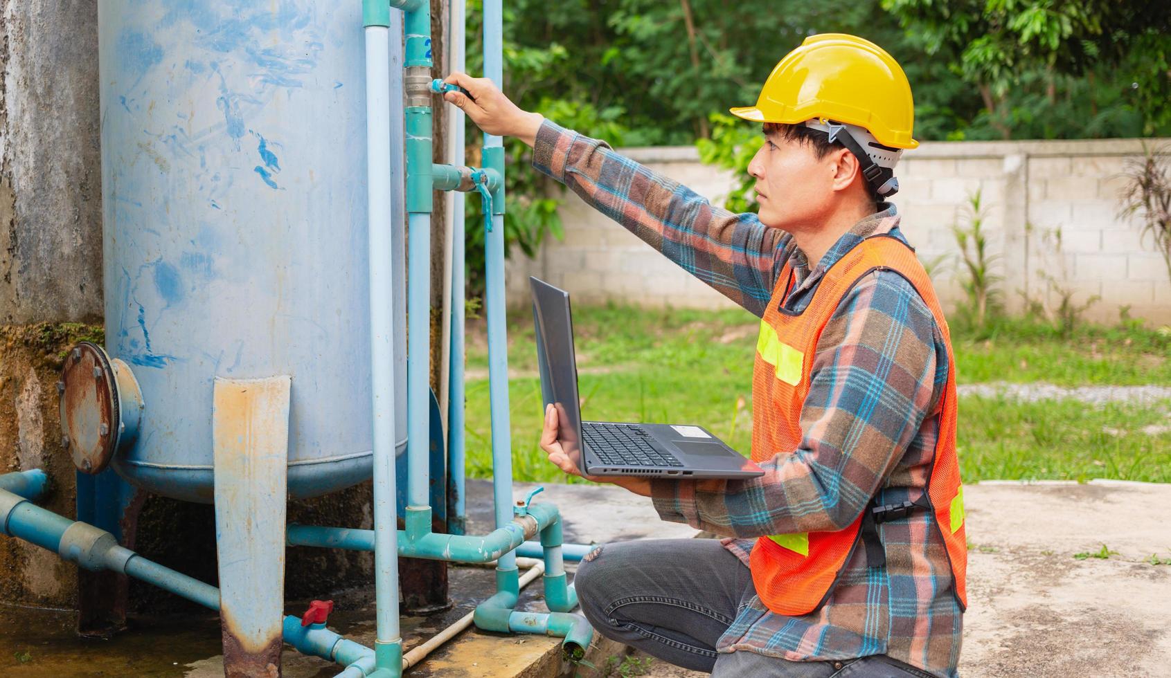 Engineer working in drinking water factory using a laptop computer to check water management system and boiler water pipe  outside the factory photo