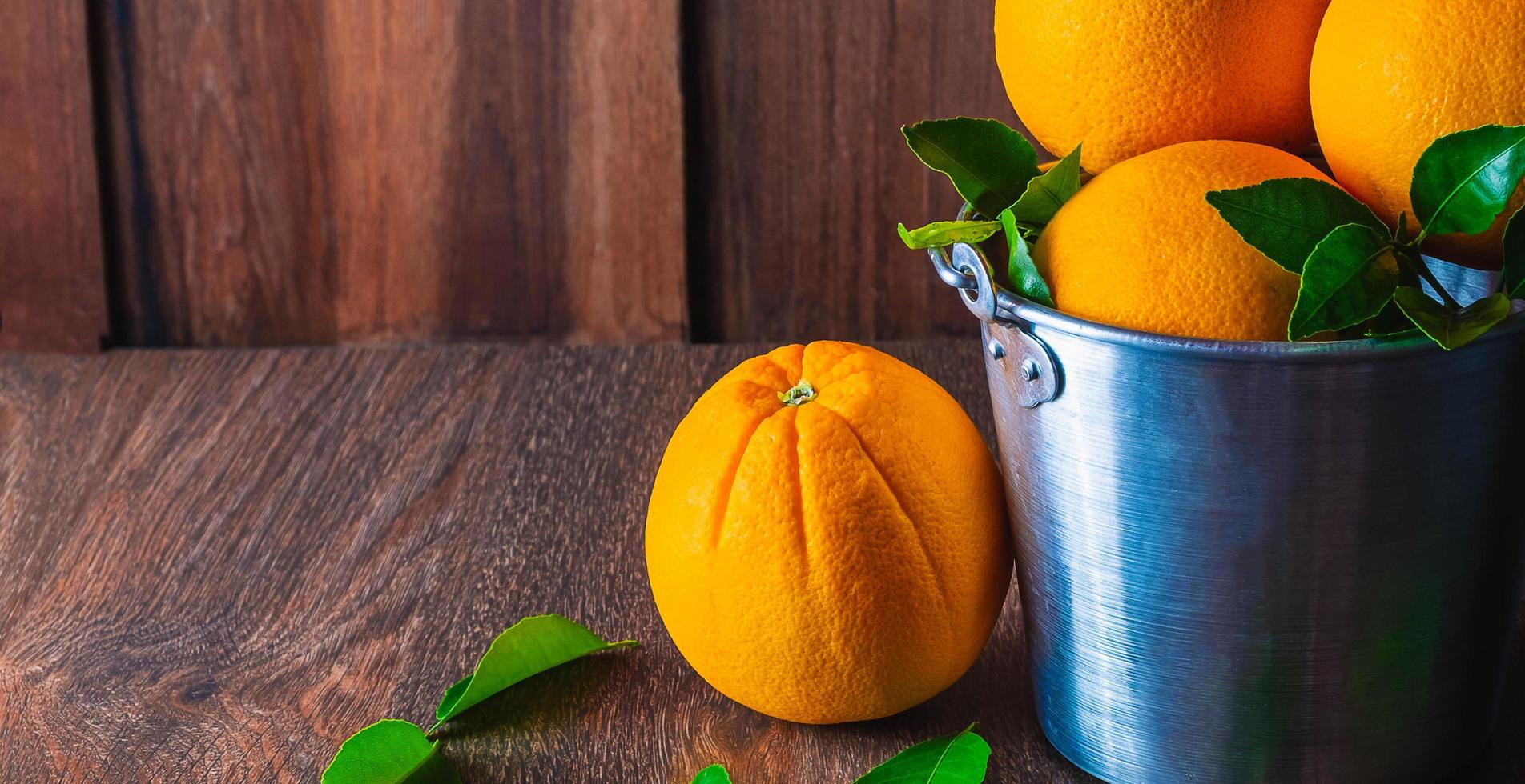 fruta naranja fresca sobre una mesa de madera y muchas naranjas en una cesta de acero inoxidable sobre fondo de madera. foto