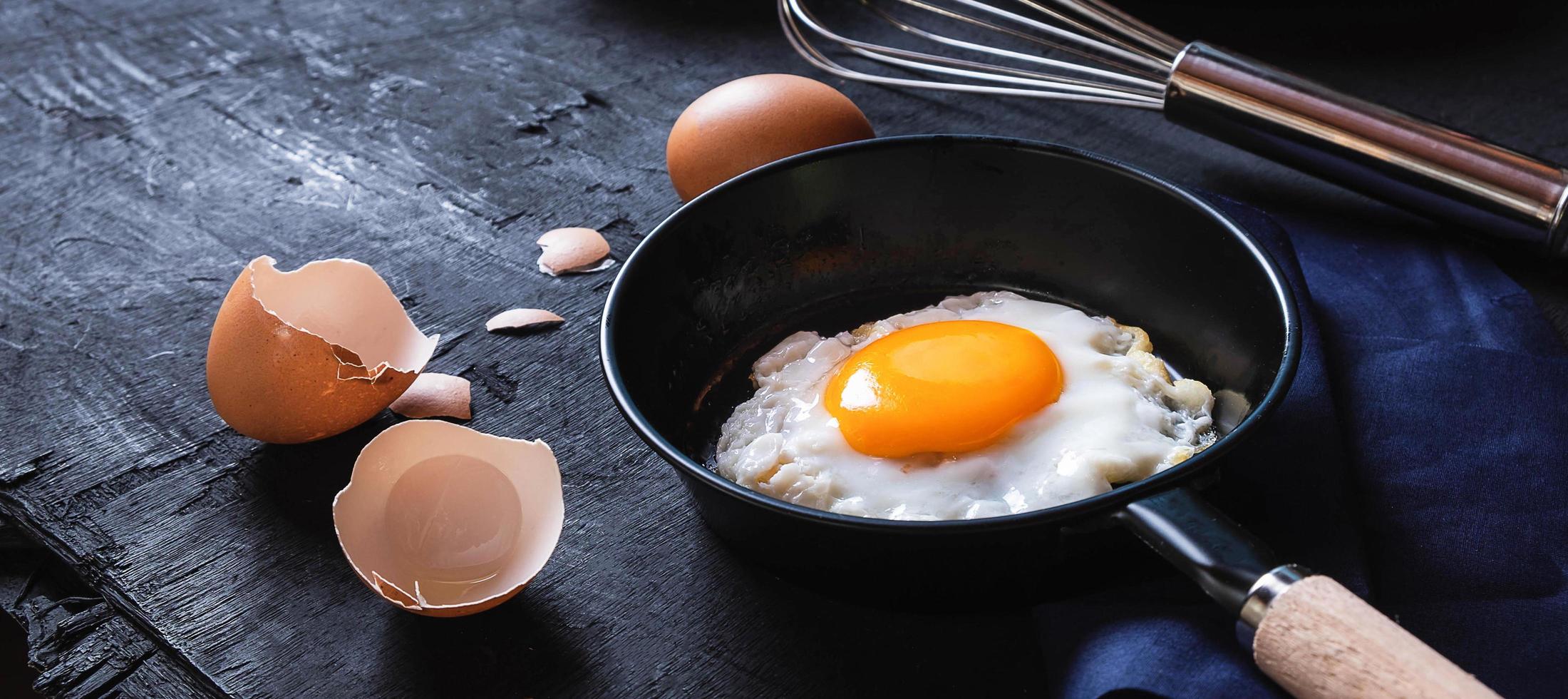 menú de cocina en la cocina huevo frito huevo en la sartén y huevos crudos frescos sobre fondo de madera negra foto