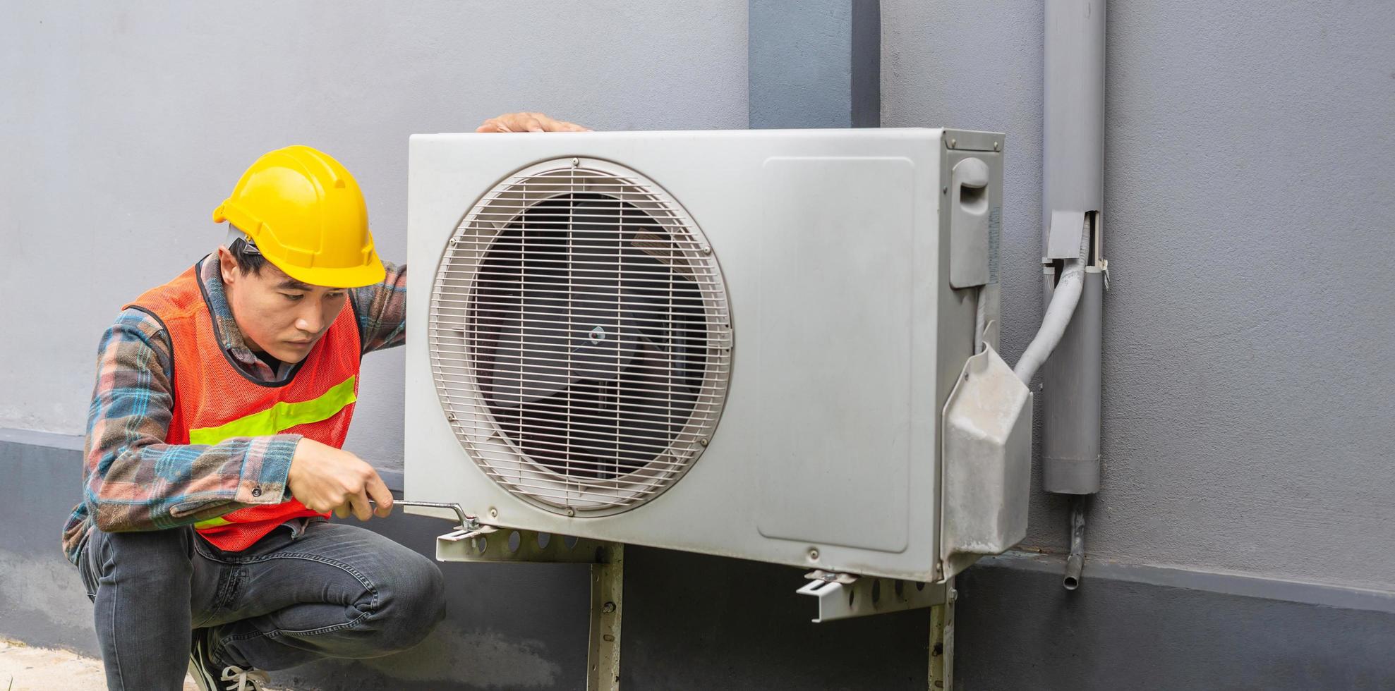 The air conditioner technician Uses a wrench to tighten the nut of the air compressor. Young Asian man repairman checking an outside air conditioner unit. photo