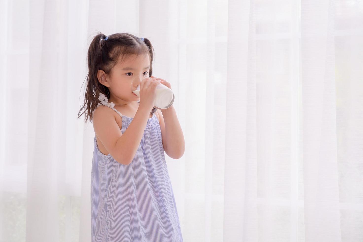 A growing Asian girl stands in her bedroom and enjoys a delicious breakfast of fresh milk photo