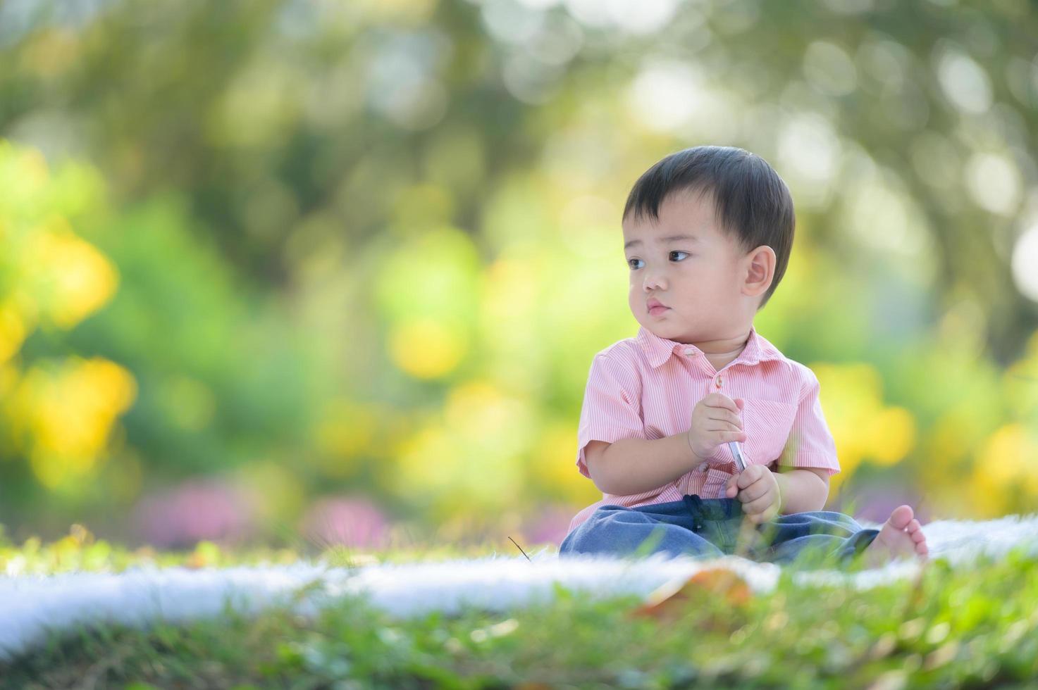 Asian boy sitting on the carpet holding a pen while learning from outside the school in the nature park photo