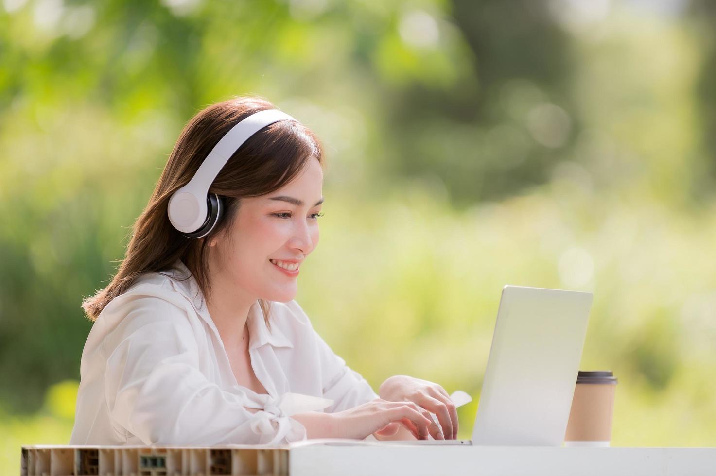 Beautiful Asian woman wearing headphones communicating via laptop in the garden photo