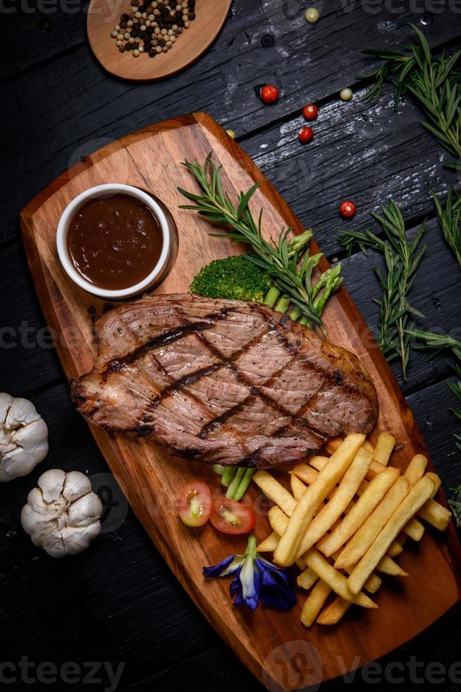 filete de ternera a la parrilla con especias y patatas fritas en una tabla de cortar de madera foto