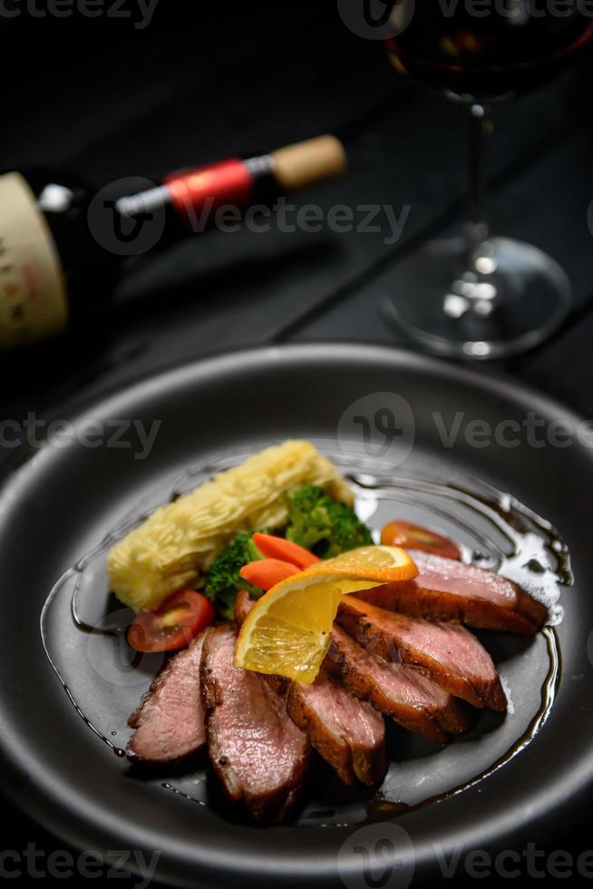 Juicy duck breast steak with caramelized fruit and orange sauce on a dark wooden floor photo