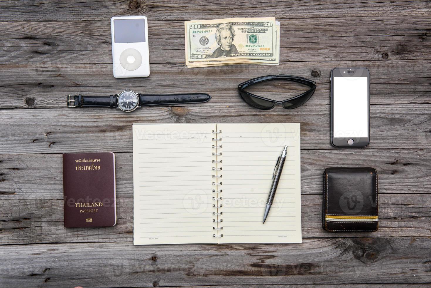 Travel things for traveling.passport, wallet, money,phone, sunglasses, watch, to-do list on a wooden table. Open notebook with white page. photo