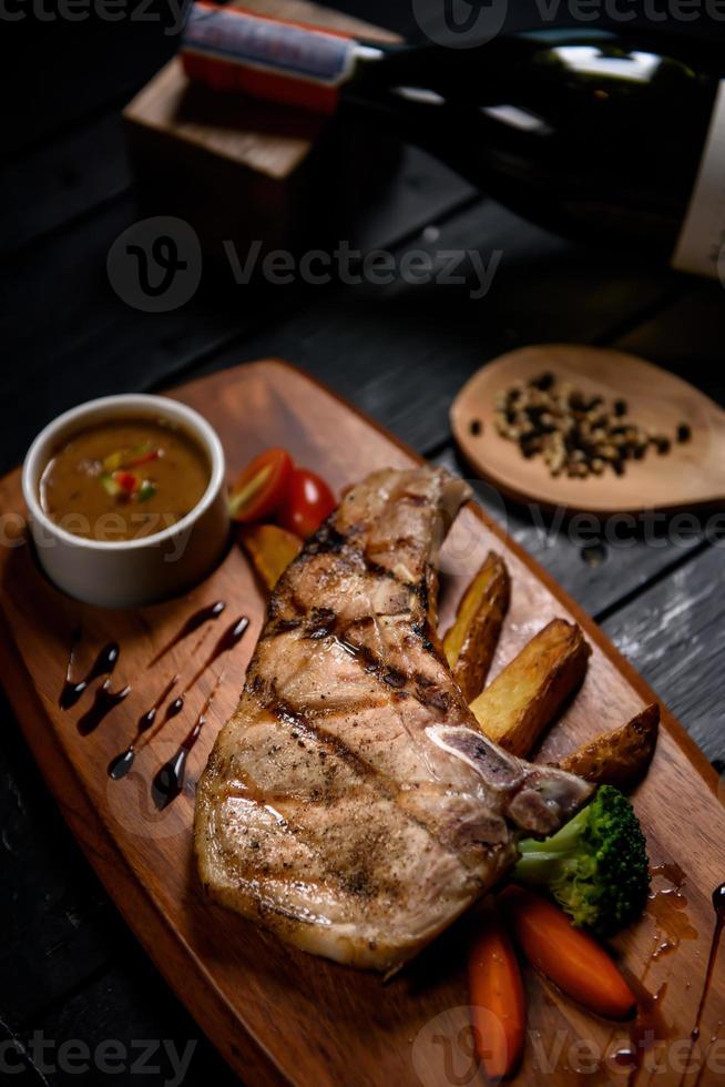 grilled pork steak on wooden plate on black background photo