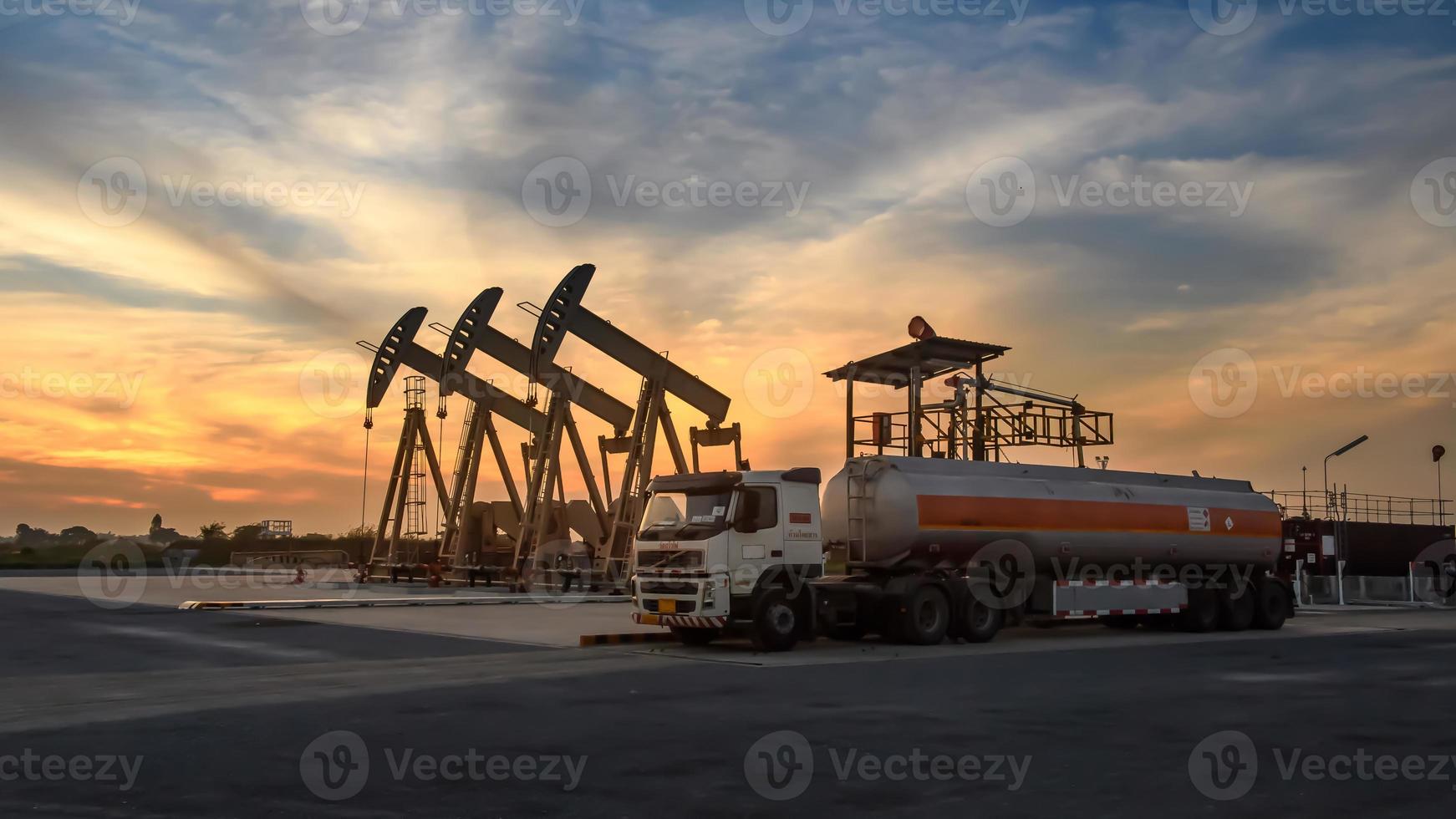 las plataformas petroleras y los camiones petroleros están trabajando o estacionados para drenar el petróleo en los campos petroleros. al atardecer o al amanecer por la tarde o por la mañana foto