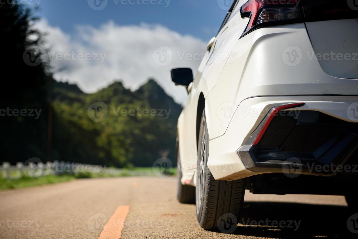 Close-up rear view of a white car with mountains and sky on the road. photo