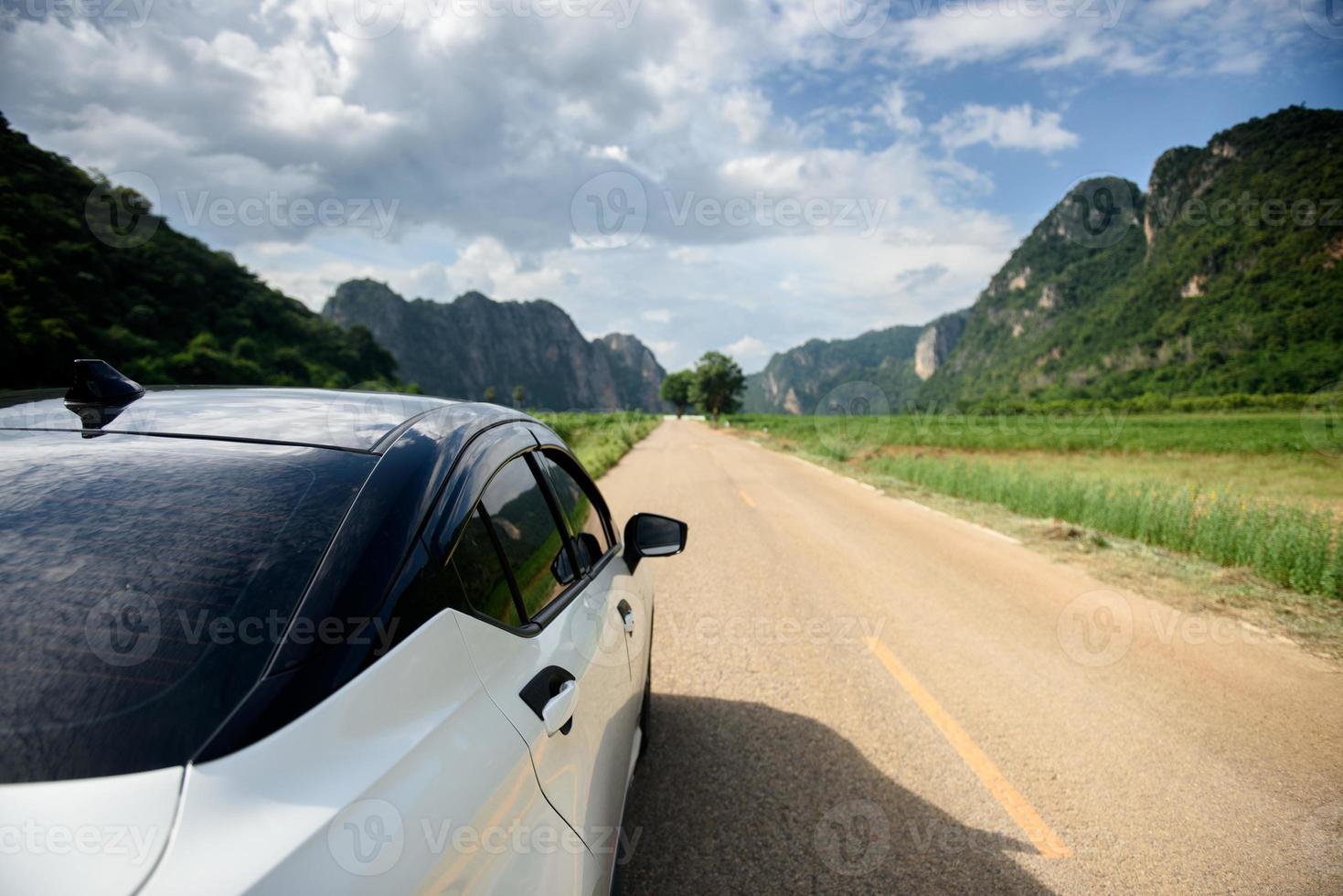 Close-up rear view of a white car with mountains and sky on the road. photo