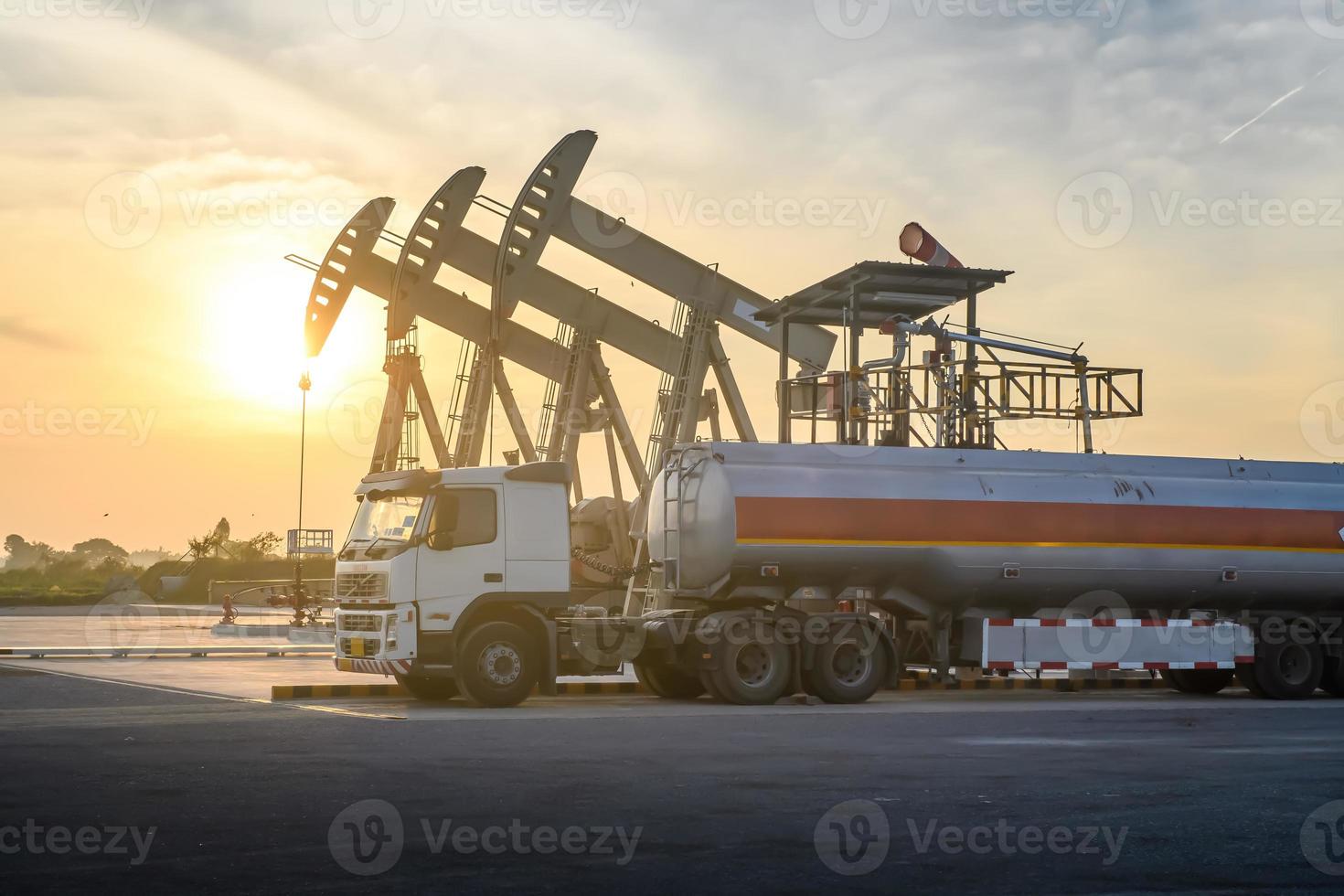 las plataformas petroleras y los camiones petroleros están trabajando o estacionados para drenar el petróleo en los campos petroleros. al atardecer o al amanecer por la tarde o por la mañana foto