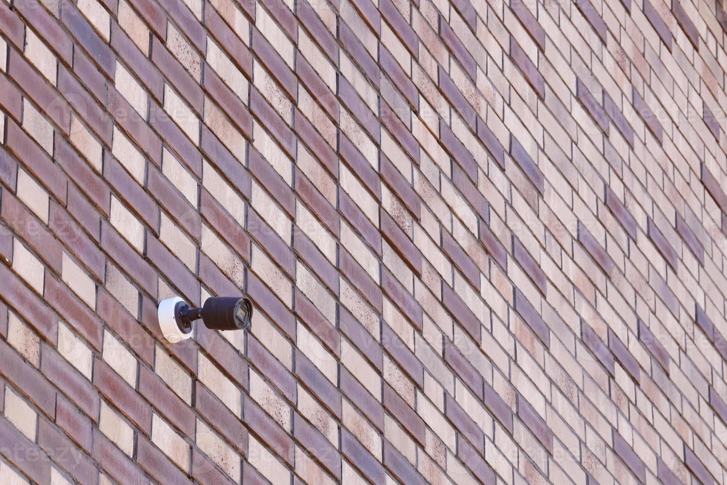 Black wireless CCTV security camera for area surveillance placed on brick wall. Surveillance cameras are modern technology to prevent thieves photo