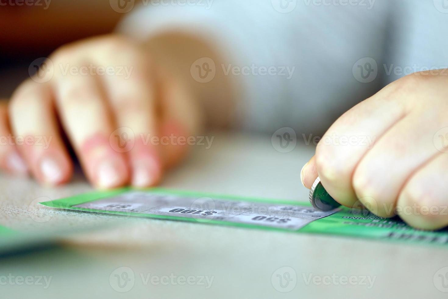 Close up view of silver coin in hand of gambler scratching fake lottery card. Lottery gambling concept, scratching cards lottery photo