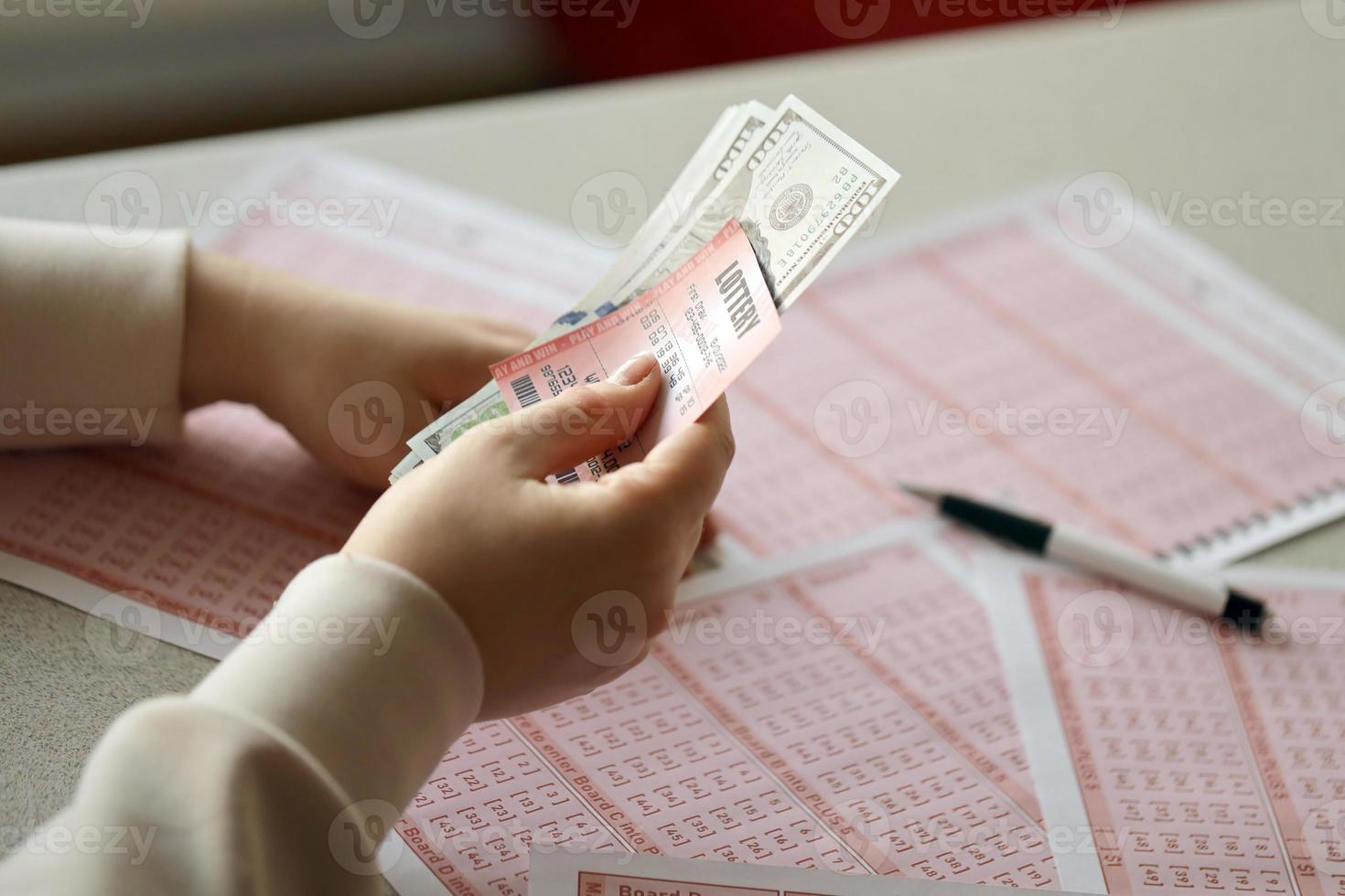 una mujer joven sostiene el billete de lotería con una fila completa de números y billetes de dólar en el fondo de las hojas en blanco de la lotería foto