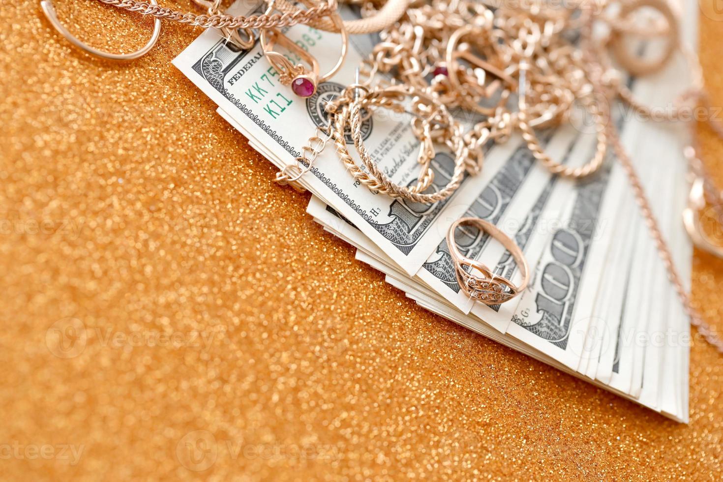 Many expensive golden jewerly rings, earrings and necklaces with big amount of US dollar bills on luxury glitter golden background surface. Pawnshop or jewerly shop photo