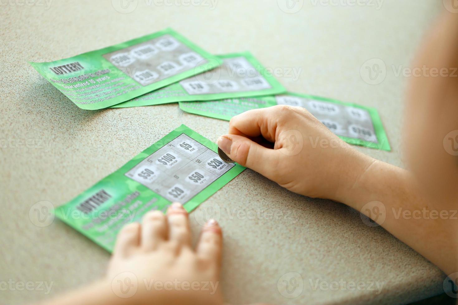 Close up view of silver coin in hand of gambler scratching fake lottery card. Lottery gambling concept, scratching cards lottery photo