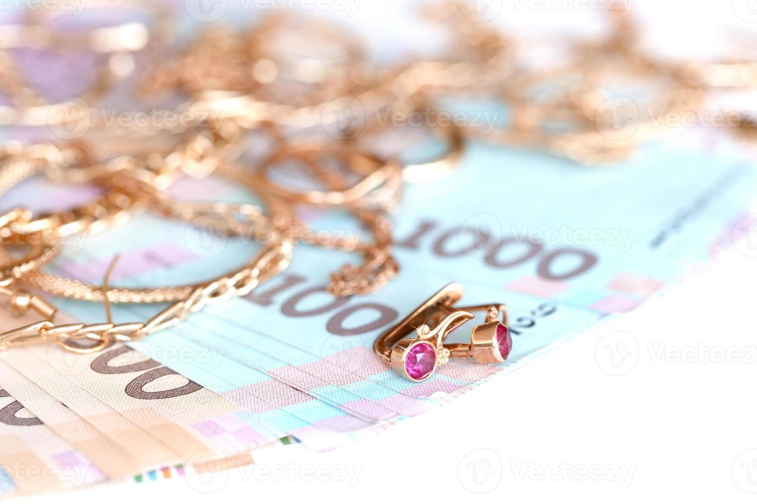 Many expensive golden jewerly rings, earrings and necklaces with big amount of Ukrainian money bills. Pawnshop or jewerly shop concept. Jewelry trading photo