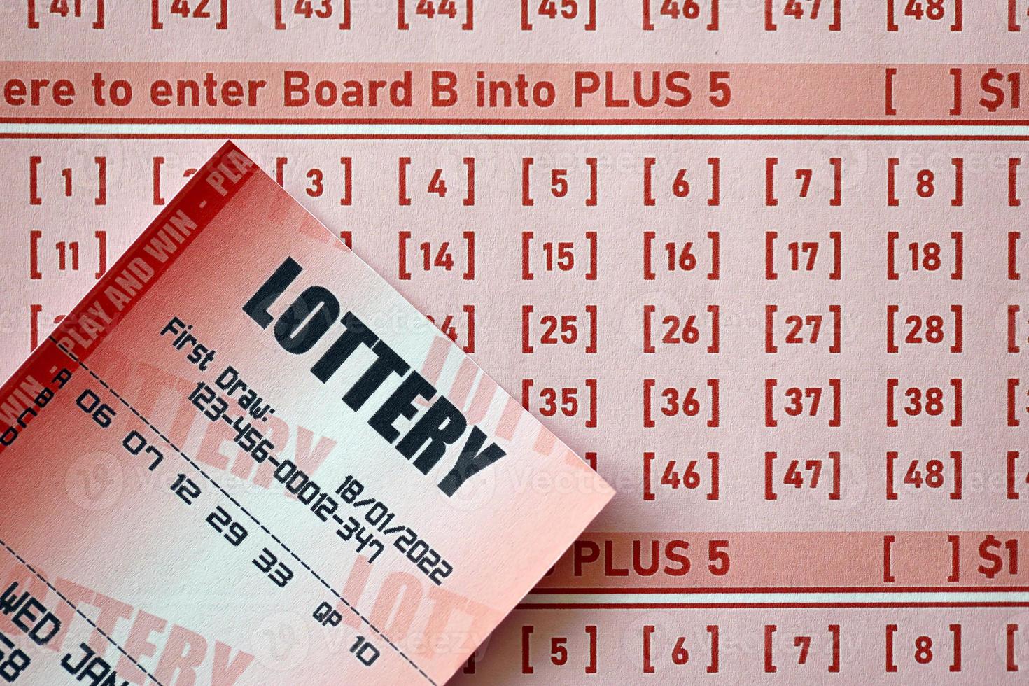 Red lottery ticket lies on pink gambling sheets with numbers for marking to play lottery. Lottery playing concept or gambling addiction. Close up photo