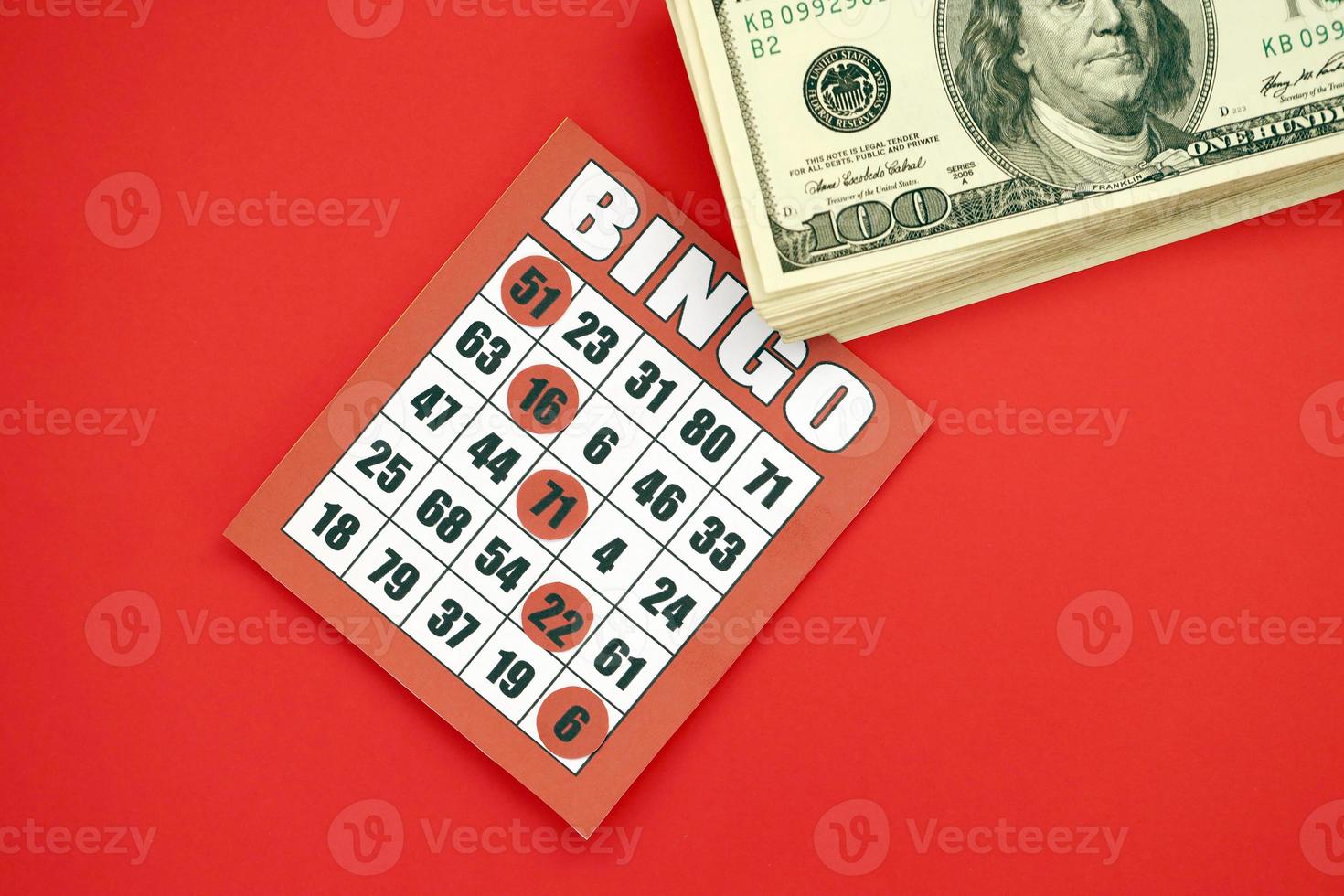 Red bingo board or playing card for winning chips and stack of dollar bills. Classic american or canadian five to five bingo card on red background photo