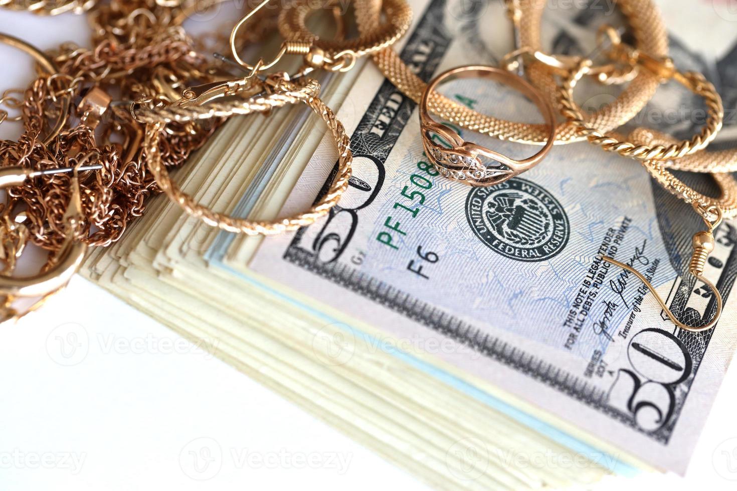 Many expensive golden jewerly rings, earrings and necklaces with big amount of US dollar bills on white background. Pawnshop or jewerly shop photo