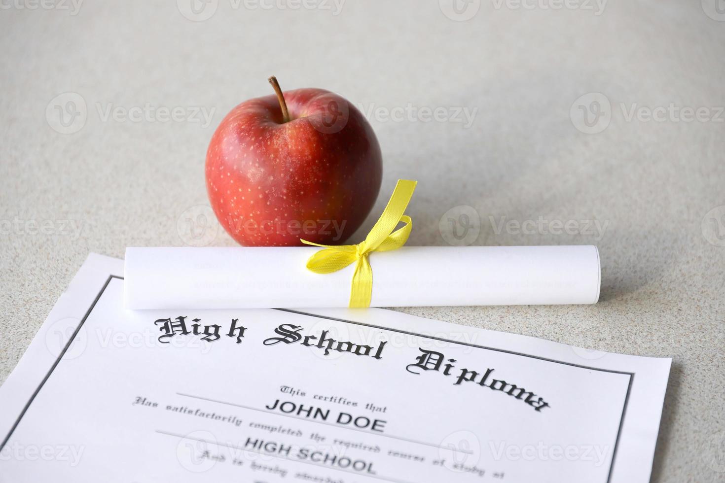 un diploma de escuela secundaria se encuentra en la mesa con un pequeño pergamino y una manzana roja. documentos educativos foto