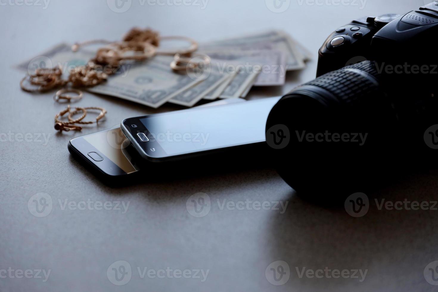 Many expensive golden jewerly rings, earrings and necklaces with big amount of US dollar bills close to smartphones and digital slr camera. Pawn shop photo