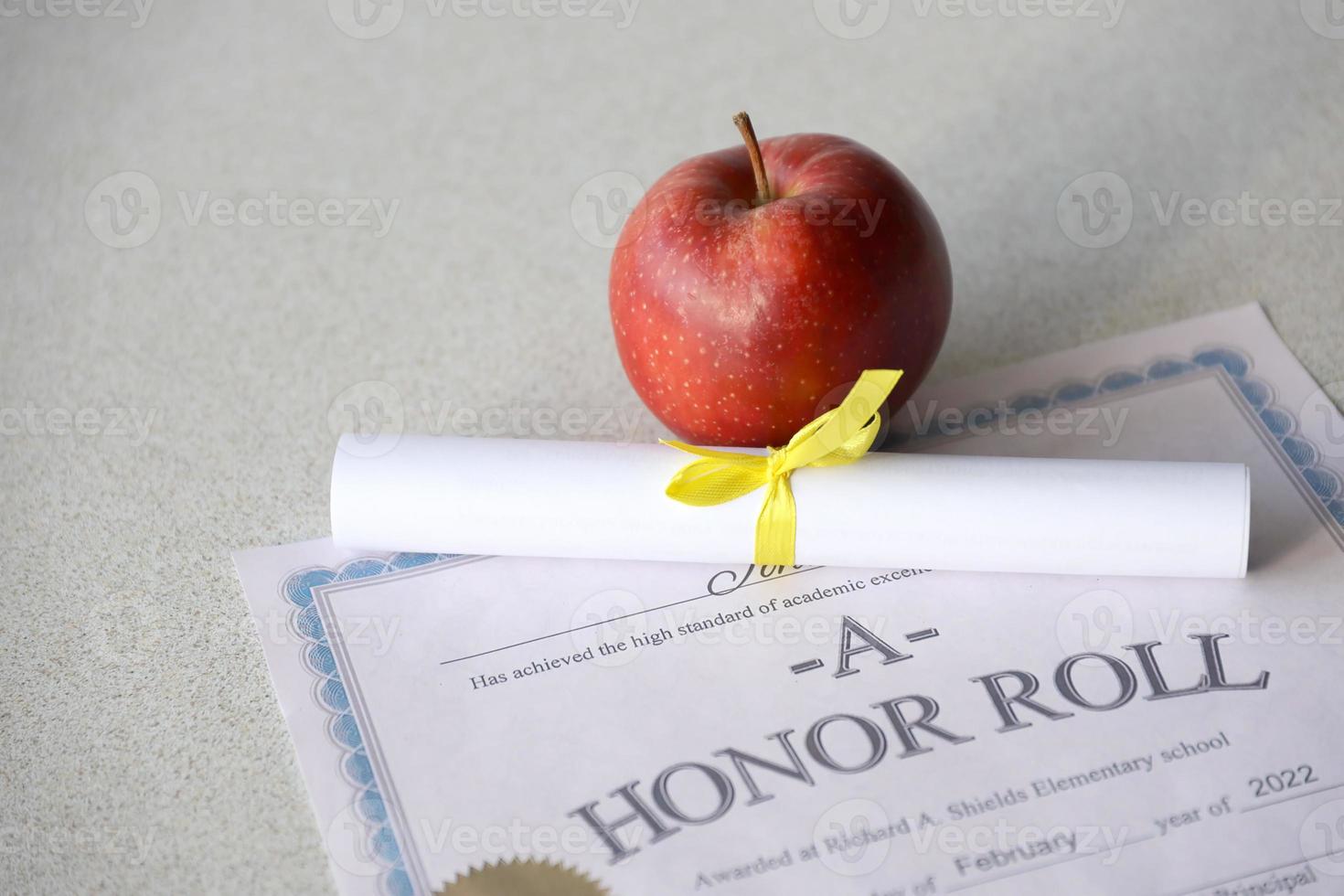 A honor roll lies on table with small scroll and red apple. Education documents photo