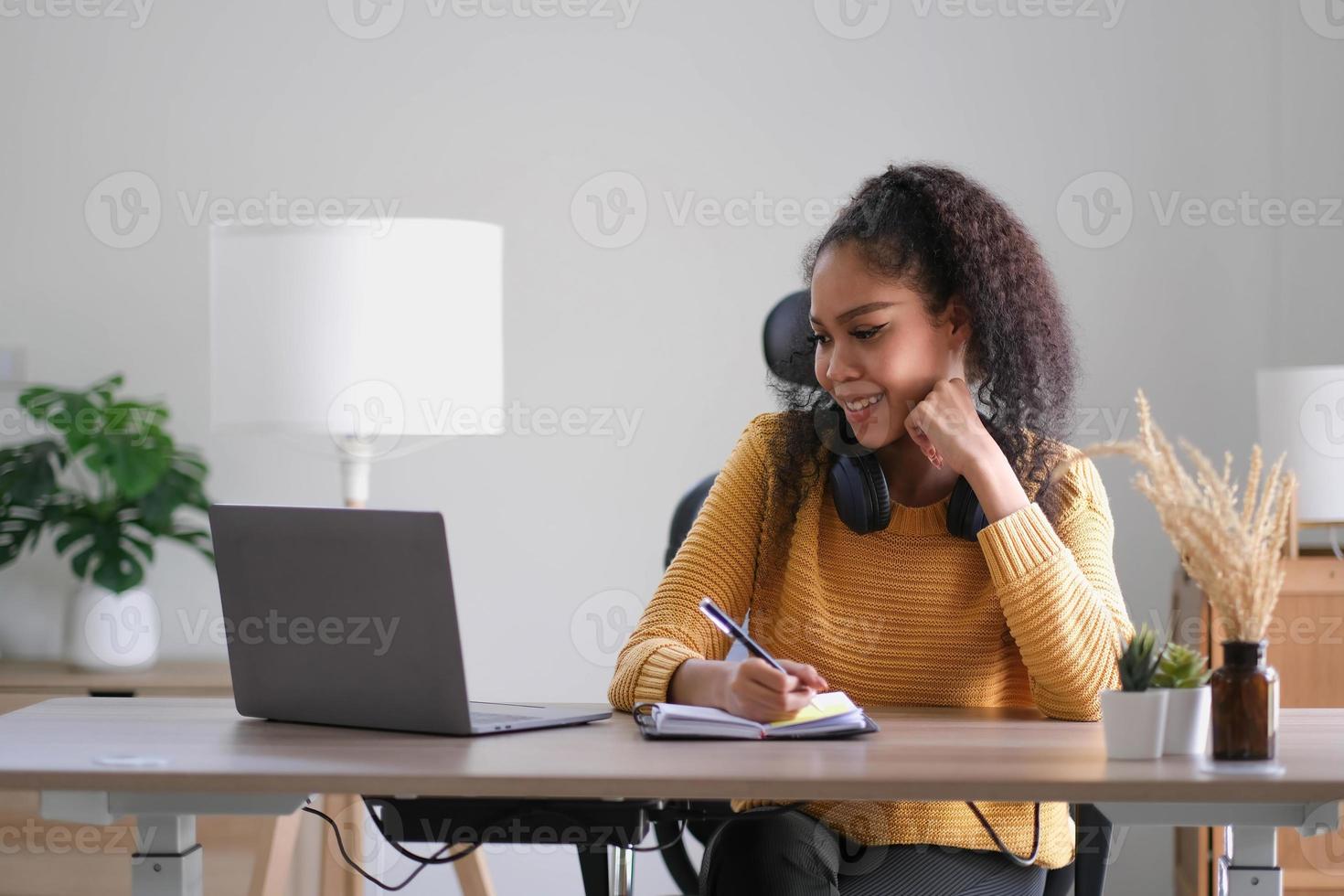 Young adult happy smiling Hispanic Asian student wearing headphones talking on online chat meeting using laptop in university campus or at virtual office. College female student learning remotely. photo