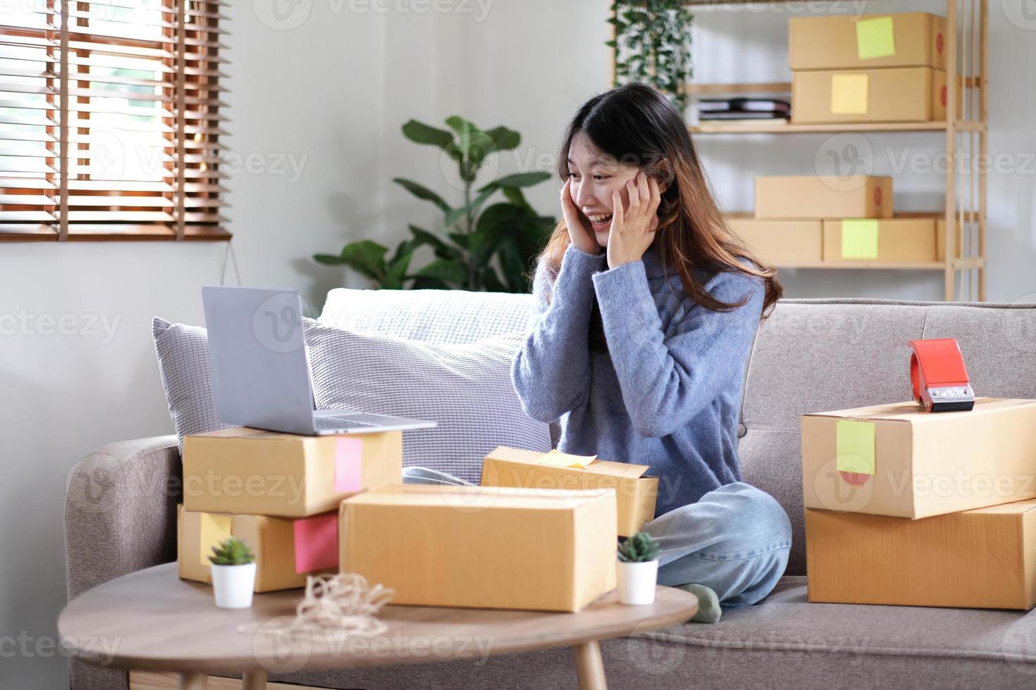 Happy young Asian woman entrepreneur, Smile for sales success after checking order from online shopping store in a smartphone at home office, Concept of merchant business online and eCommerce photo