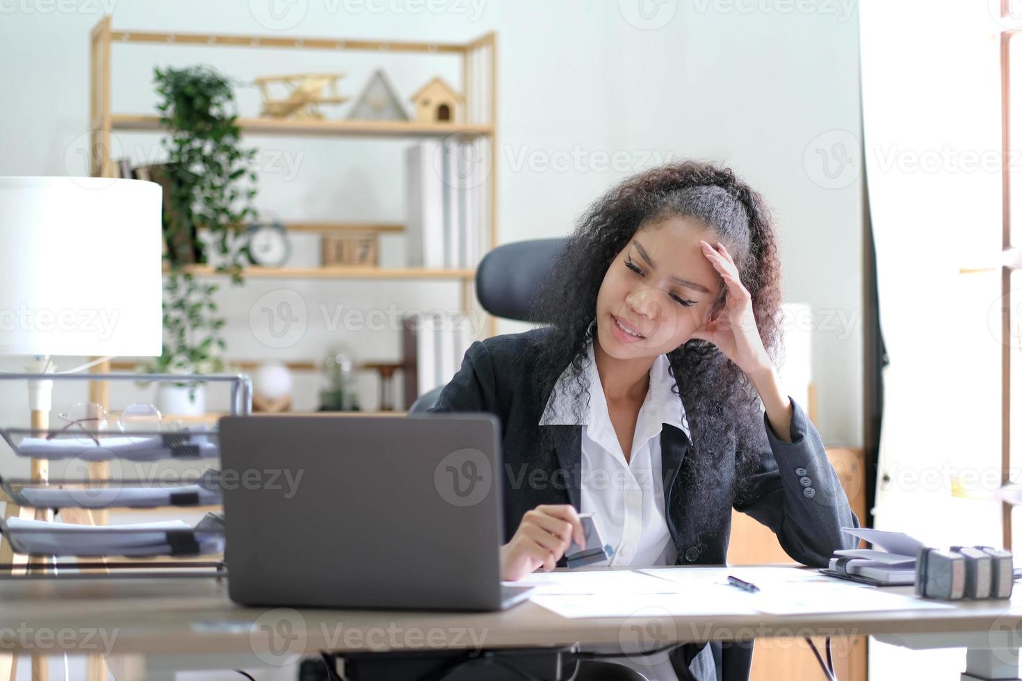 empresaria afroamericana seria sentada en la mesa mirando la pantalla del portátil. mujer étnica lee mensajes de correo electrónico con noticias importantes, documentos comerciales en línea, chatea con clientes que trabajan de forma remota foto