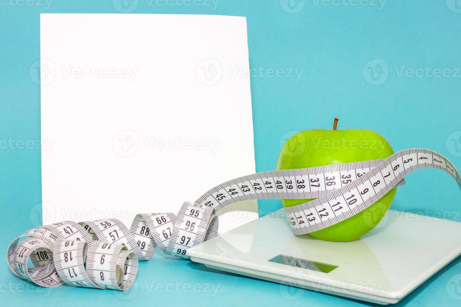 centimeter tape around green apple on scales isolated on blue background with place for text. concept of proper nutrition, diet photo