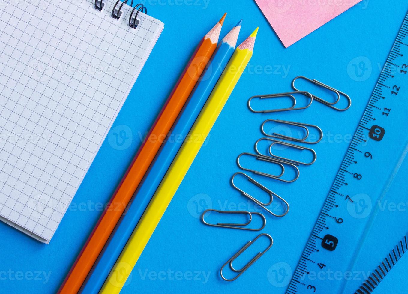 papelería escolar sobre un fondo azul. conjunto geométrico, regla, lápices, bloc de notas, clips de papel. el concepto de educación. foto