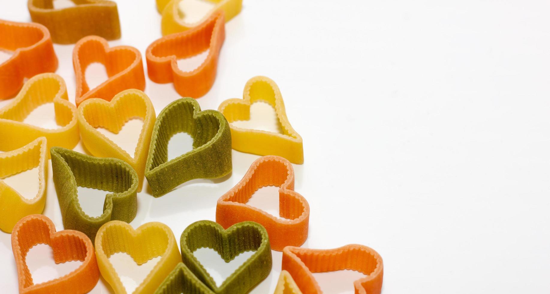 multicolored pasta in the shape of a heart on a white background. holiday and cooking concept, romantic food, photo