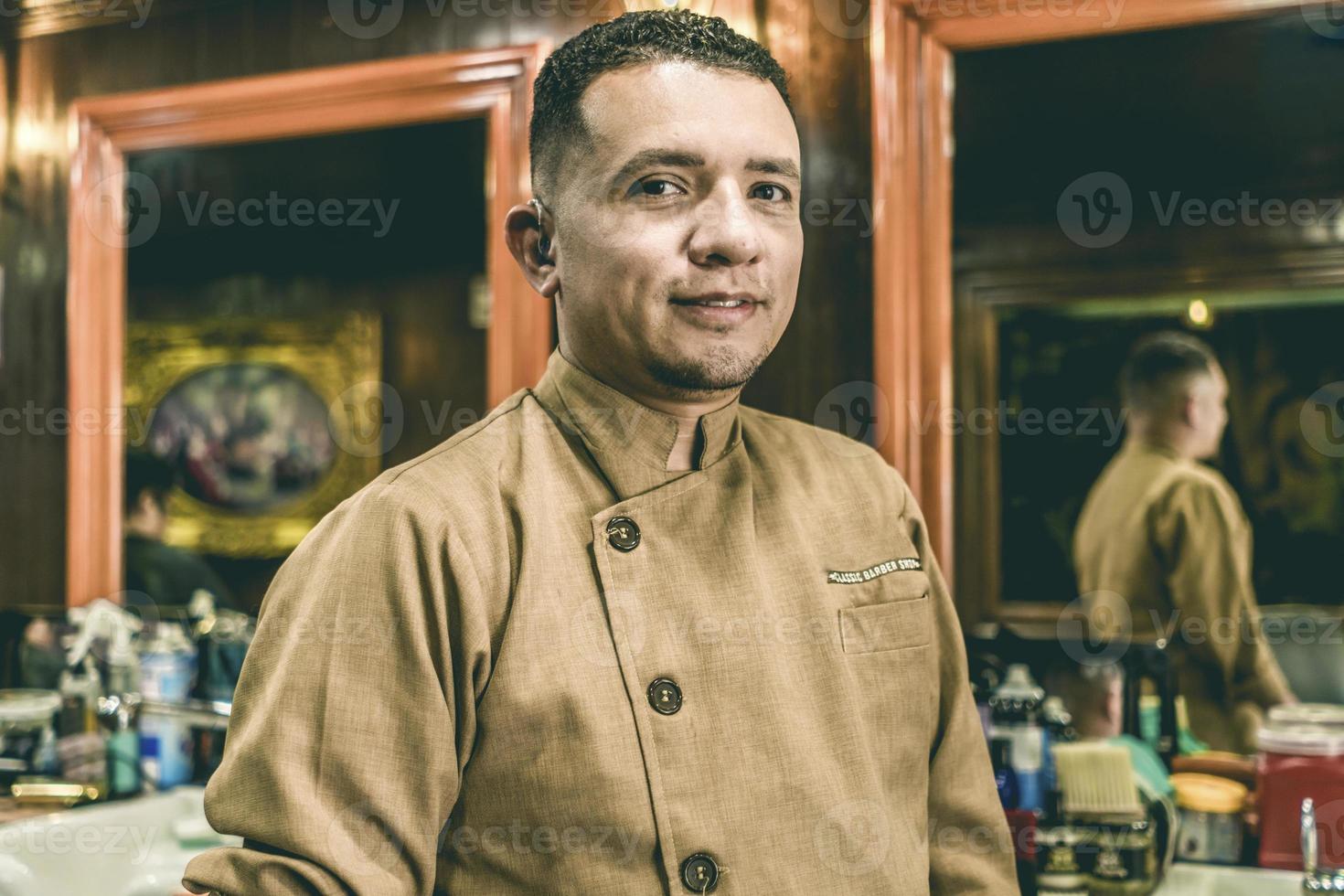 Deaf young barber with hearing aid looks at camera. photo