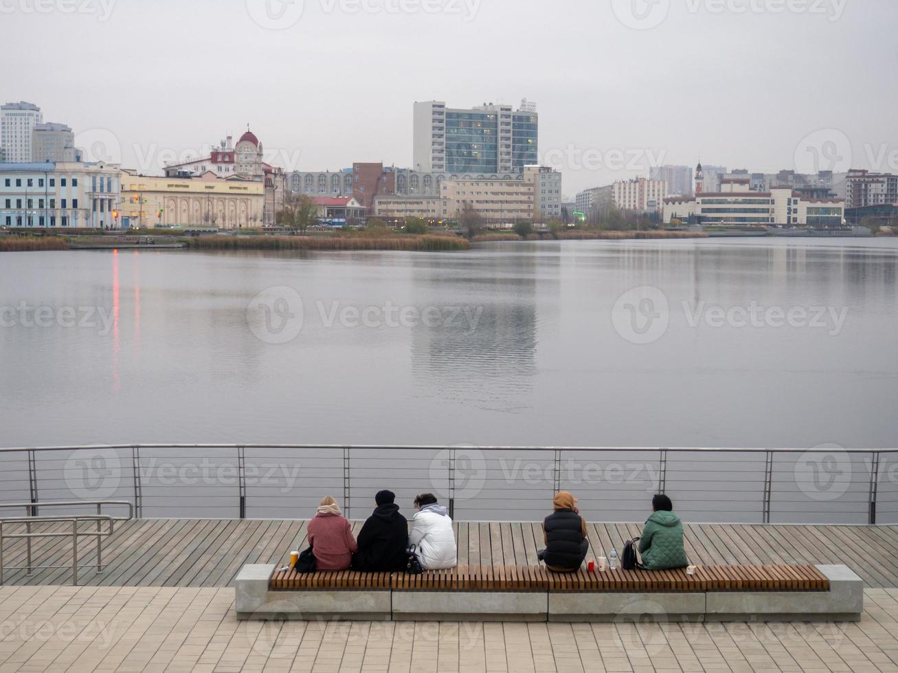 People sit on a bench on an autumn day and admire the surface of the lake. photo