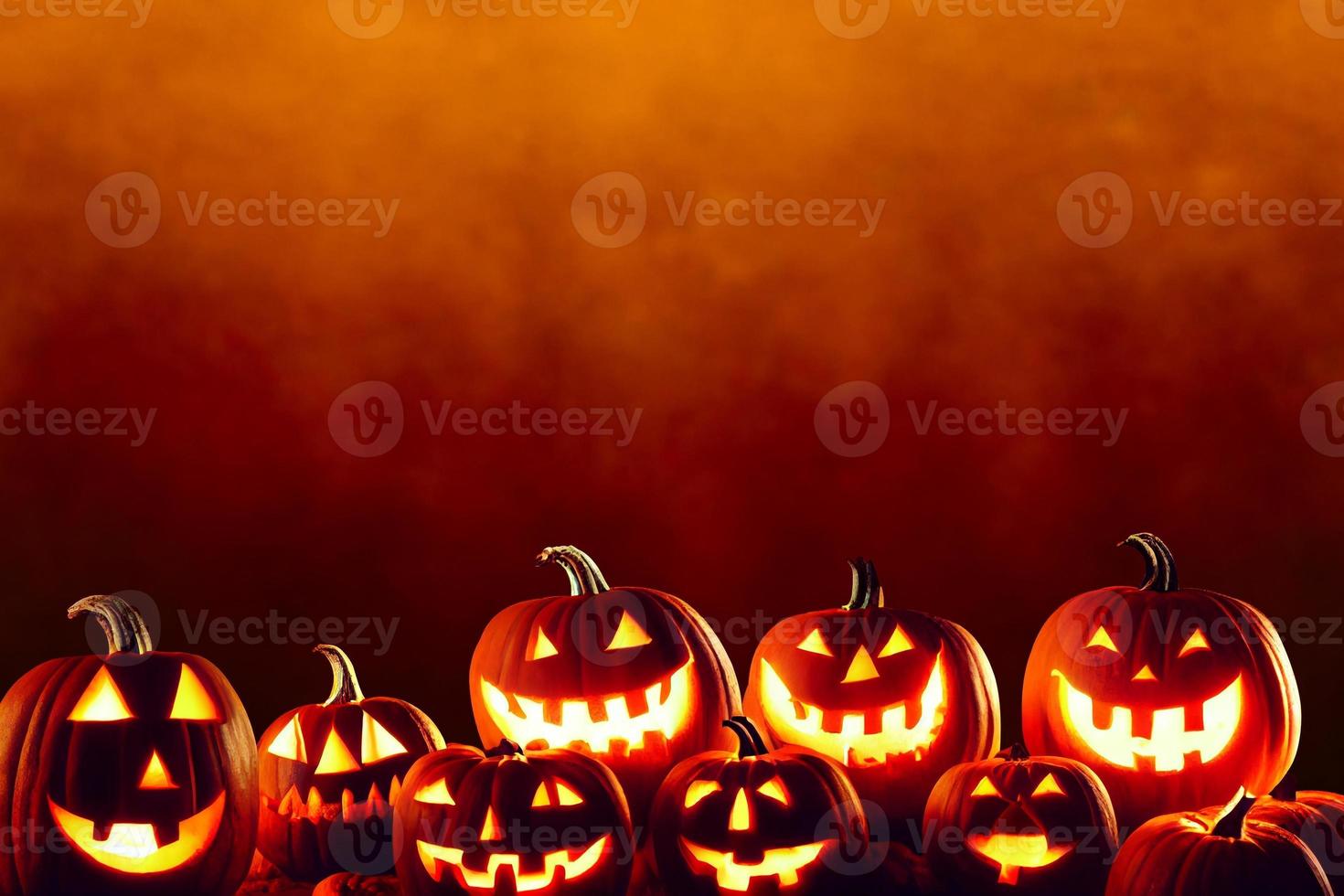 una fila de calabazas de halloween jack olantern talladas a lo largo de la parte inferior de la imagen contra un fondo grunge naranja oscuro foto