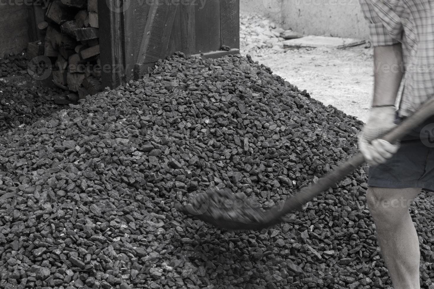 A worker with a shovel unloads black coal against the background of a large pile of coal. Energy crisis. Soft focus. photo