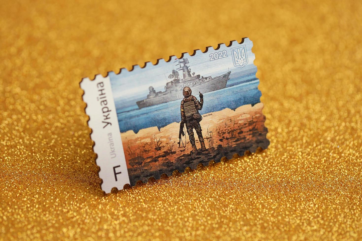 TERNOPIL, UKRAINE - SEPTEMBER 2, 2022 Famous Ukrainian postmark with russian warship and ukrainian soldier as wooden souvenir on golden glitter background photo